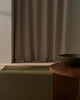 Brown curtain in a room with a wooden table and bowl and a designer wool rug
