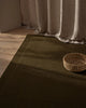 The Cassio Jasper NZ wool floor rug in a deep olive shade seen with a linen curtain