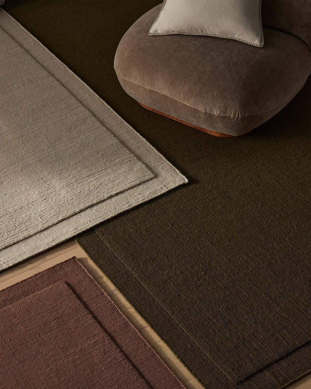 Three NZ wool rugs in beige, chocolate brown and burgundy with a brown chair int he background