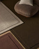 Three NZ wool rugs in beige, chocolate brown and burgundy with a brown chair int he background