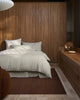 Modern bedroom with wooden wardrobe and bed, and a warm toned brown floor rug. 