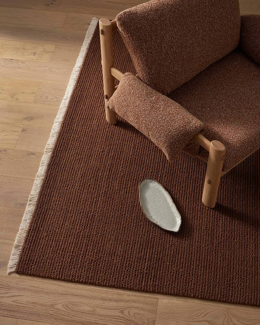 Brown textured rug with a wooden chair and a small white dish on a wooden floor.