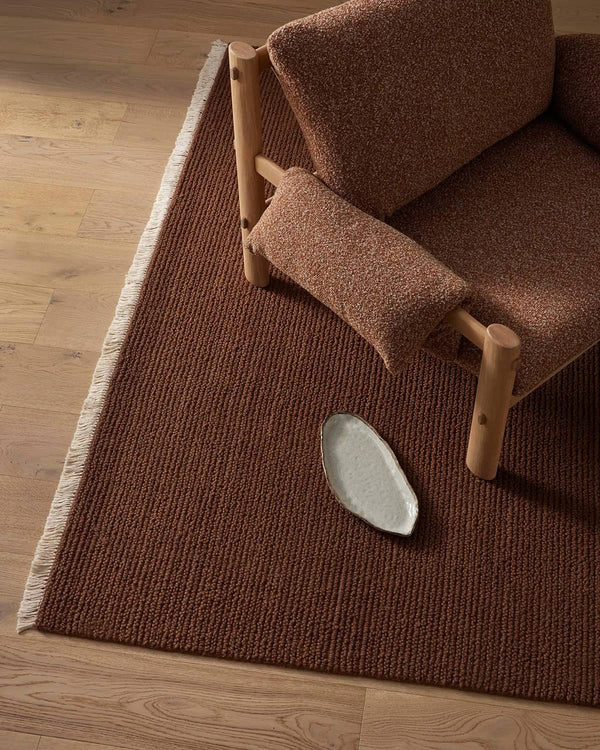 Brown textured rug with a wooden chair and a small white dish on a wooden floor.