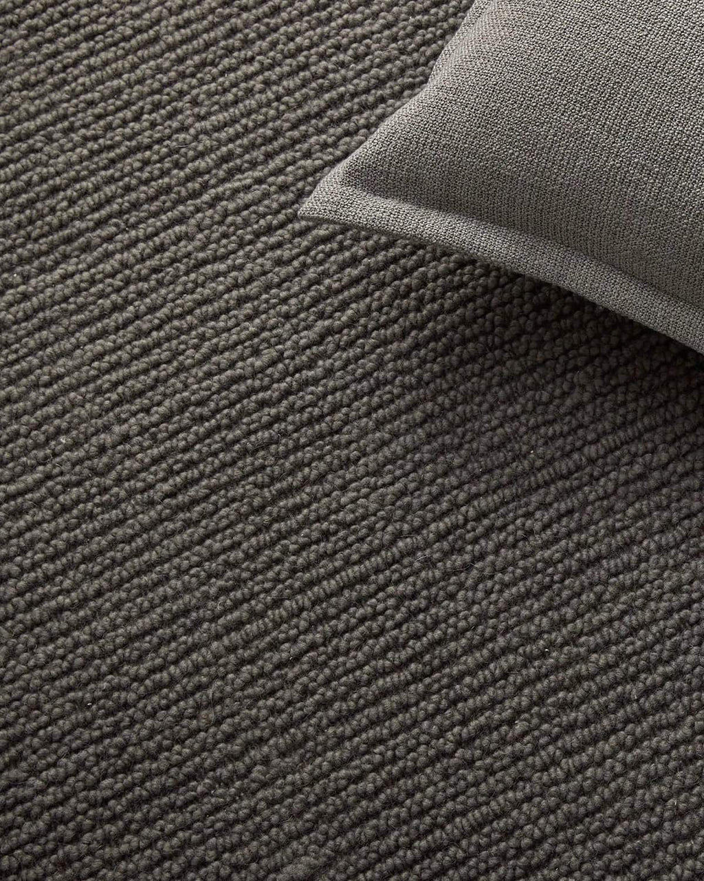 Gray textured rug with a corner of a gray pillow visible