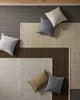 Collection of cool toned wool area rugs with variously colored cushions on a wooden floor.