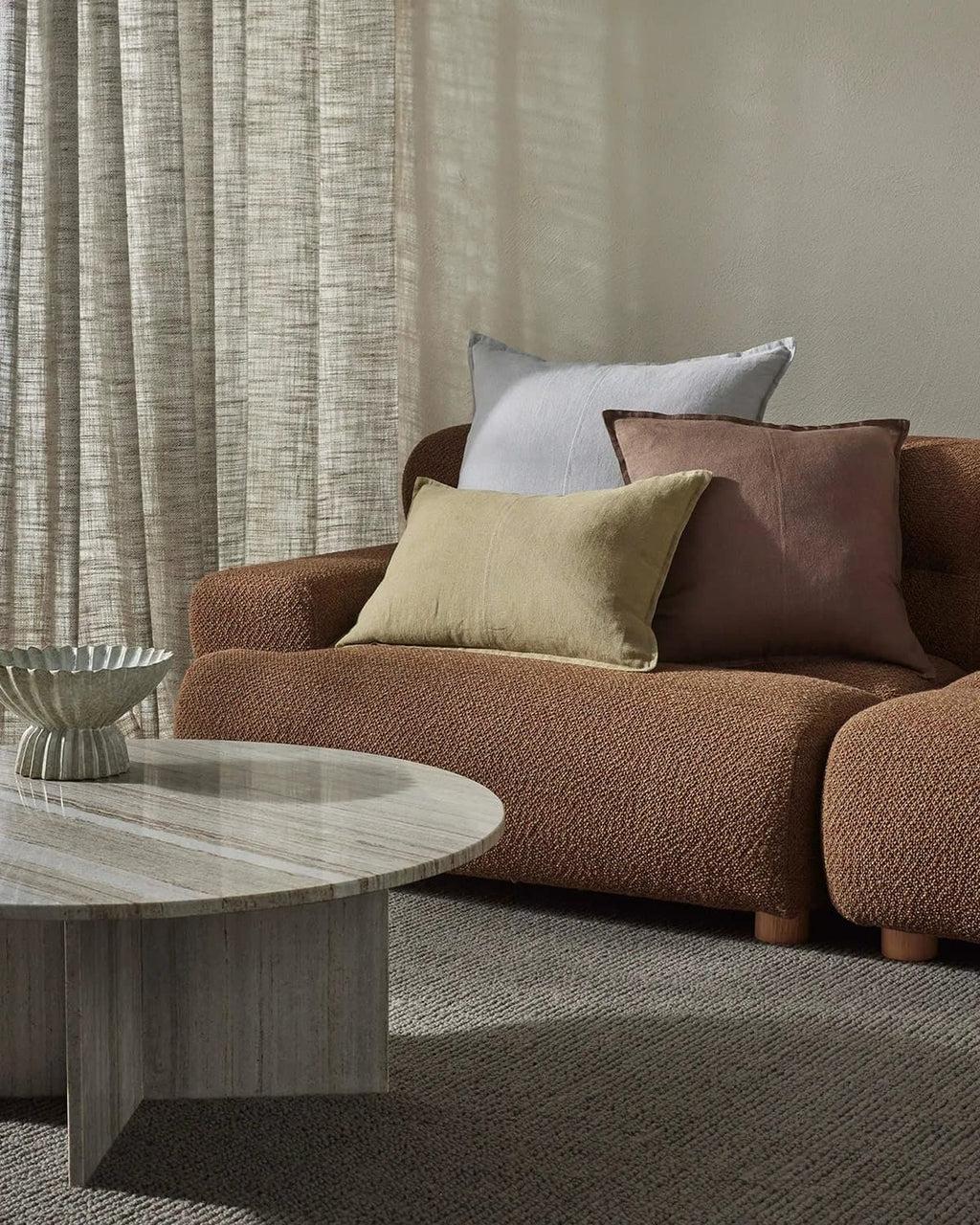 Brown sofa with decorative pillows in a living room setting with a grey textural floor rug. 