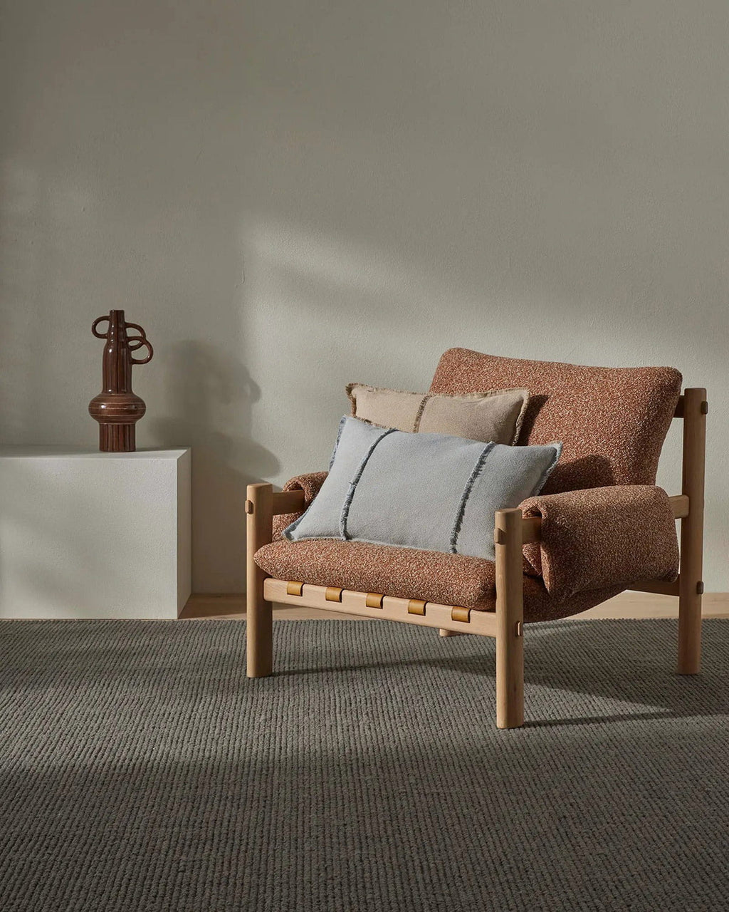 Brown armchair with cushions in a minimalistic room, with a textural grey floor rug. 