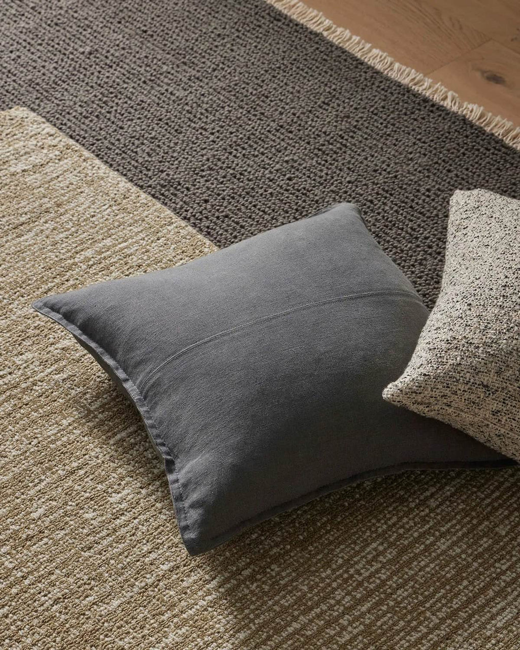 Gray pillow on a textured grey rug with another pillow partially visible