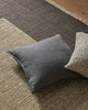 Gray pillow on a textured grey rug with another pillow partially visible