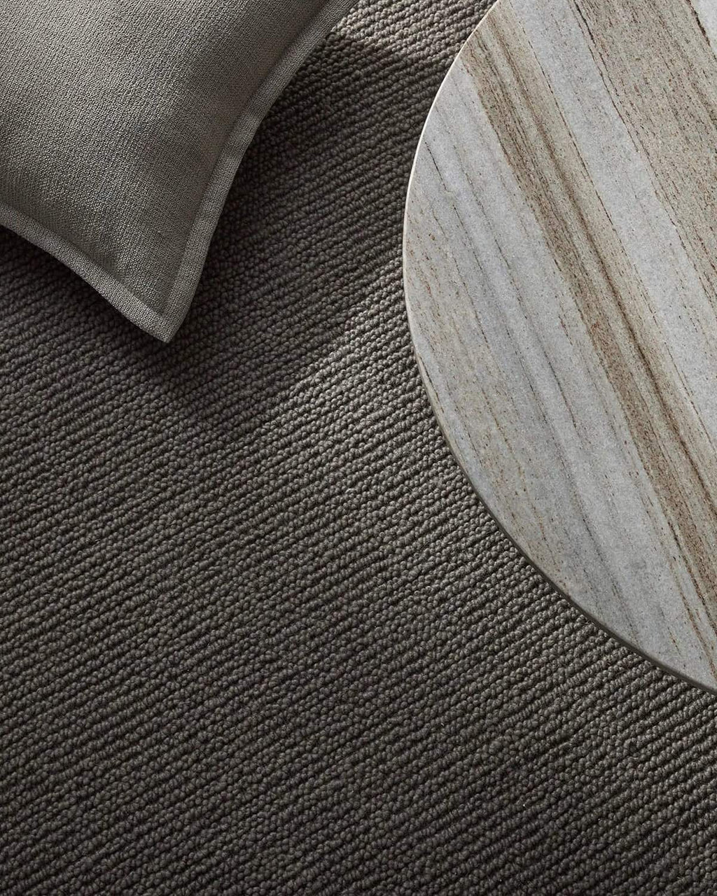 Close-up of a textured dark gray rug with a round wooden side table.