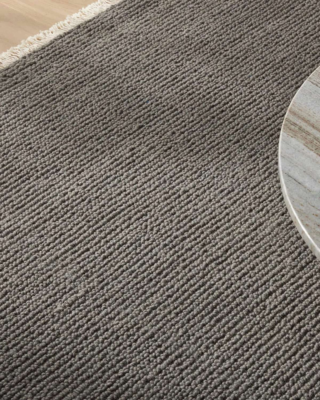 Close-up of a textured grey-toned rug with a wooden floor corner.