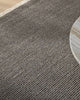 Close-up of a textured grey-toned rug with a wooden floor corner.