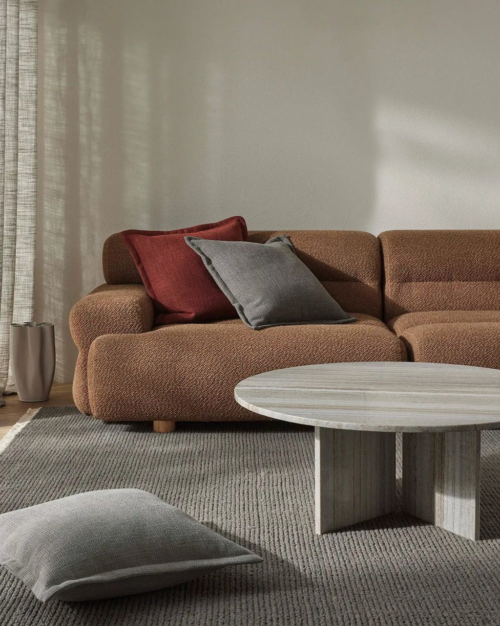 Brown sectional sofa with red and gray cushions in a living room setting with a textural floor rug in cool grey tones.