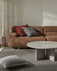 Brown sectional sofa with red and gray cushions in a living room setting with a textural floor rug in cool grey tones.