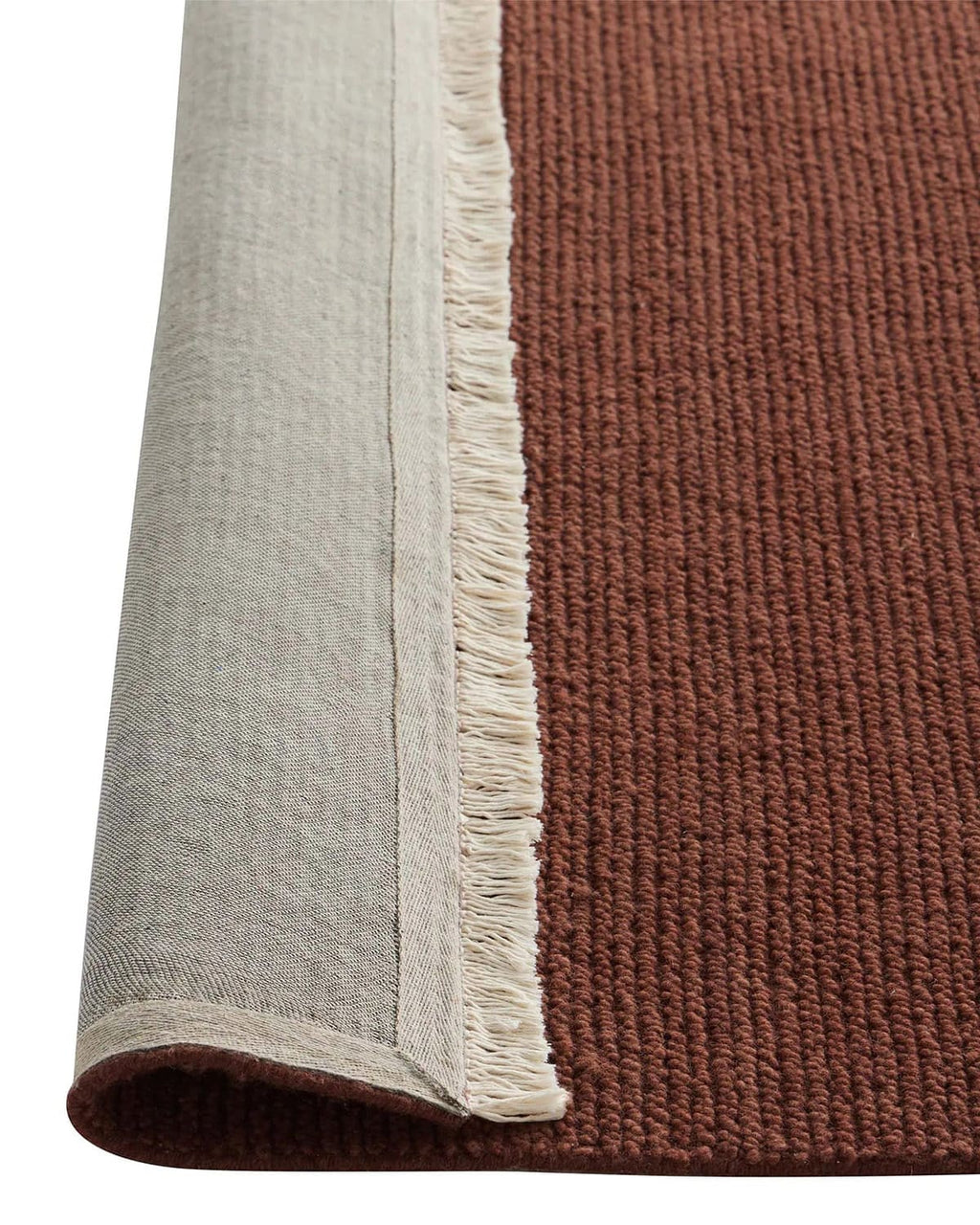 Close-up of a red rug with fringed edges, one corner lifted to show the underside.