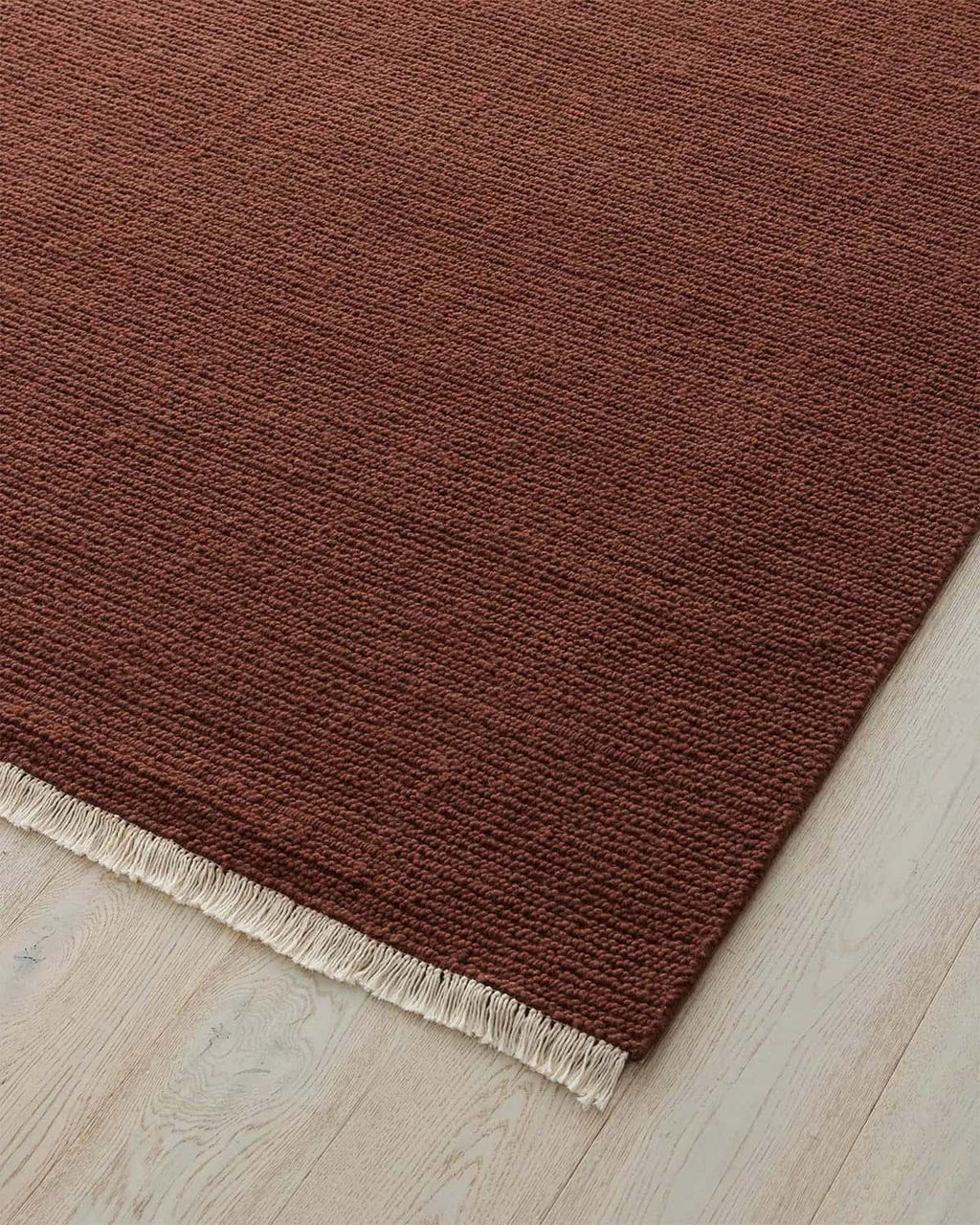 Red brown 100% wool floor rug with a textured surface on a light wood floor