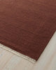 Red brown 100% wool floor rug with a textured surface on a light wood floor