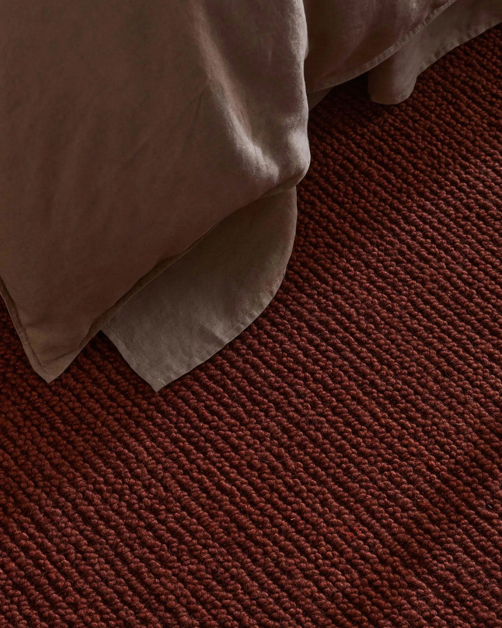 Close-up of a textured red brown rug with a corner of beige fabric.