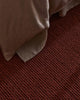 Close-up of a textured red brown rug with a corner of beige fabric.