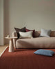 Beige sofa with colorful cushions in a minimalistic living room with a textural dark red-brown floor rug.