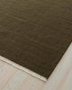 Green brown textured rug with white fringe on a light wood floor