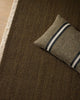 Green brown 100% wool textured rug with a pillow featuring stripes on a wooden floor.