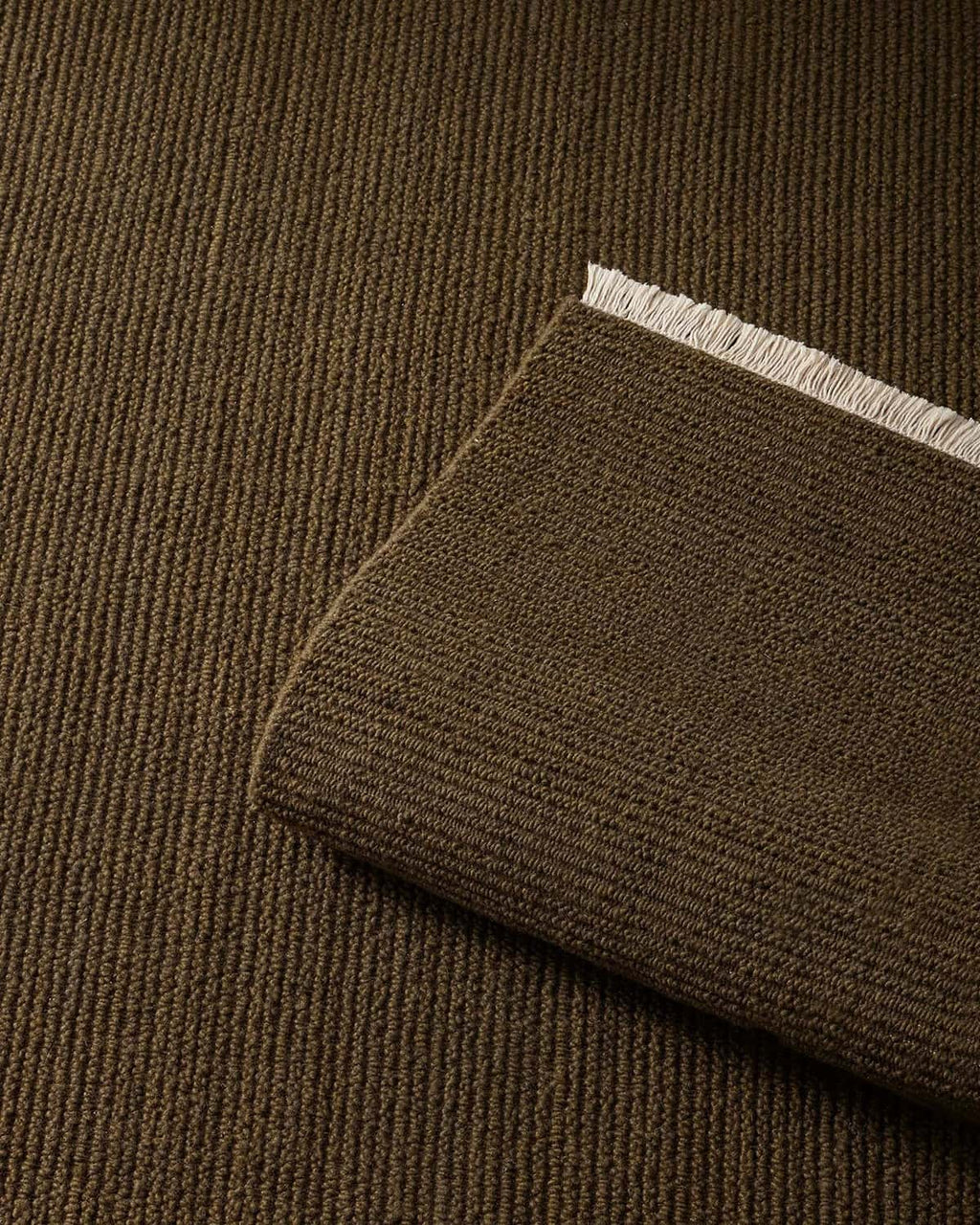 Close-up of a brown-green 100% wool textural floor rug with a sample laid atop it. 