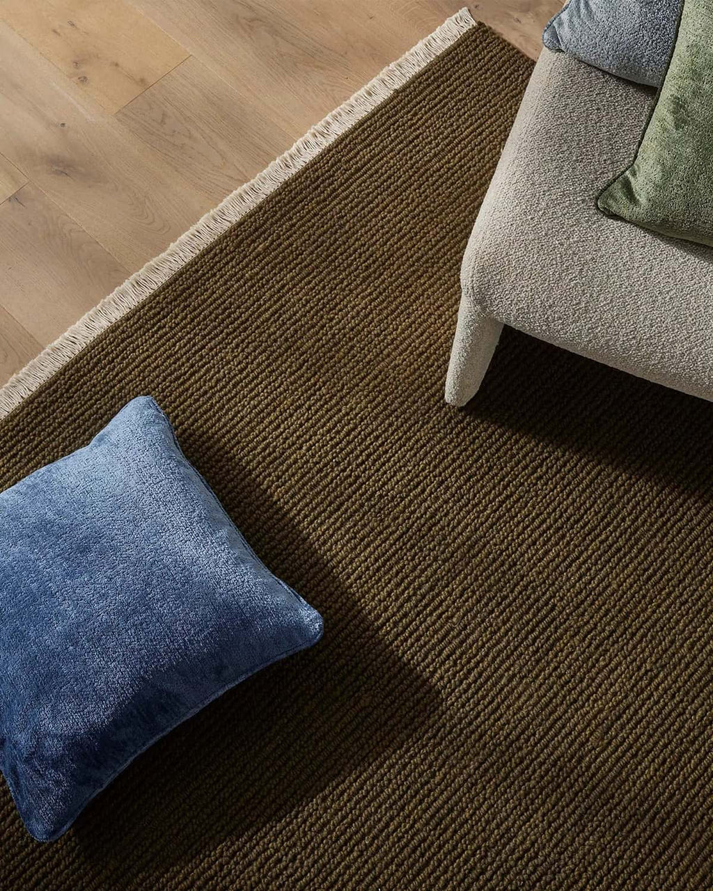 Brown-green textured rug with a blue pillow on a wooden floor