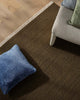 Brown-green textured rug with a blue pillow on a wooden floor