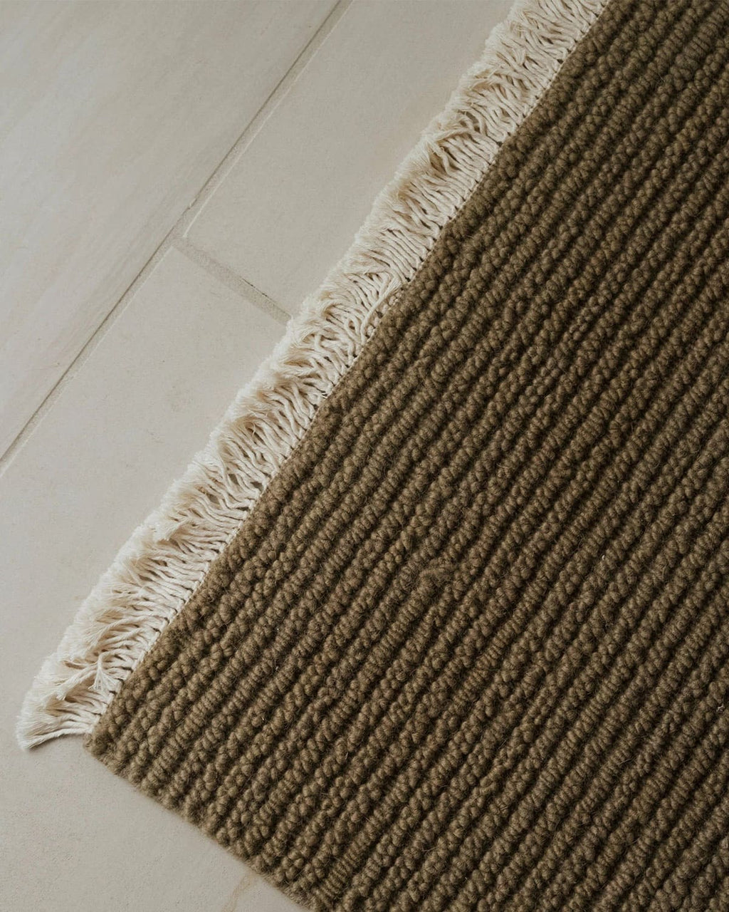 Brown textured rug with white fringe on a light wooden floor