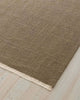 Brown textured rug with a fringed edge on a light wood floor.
