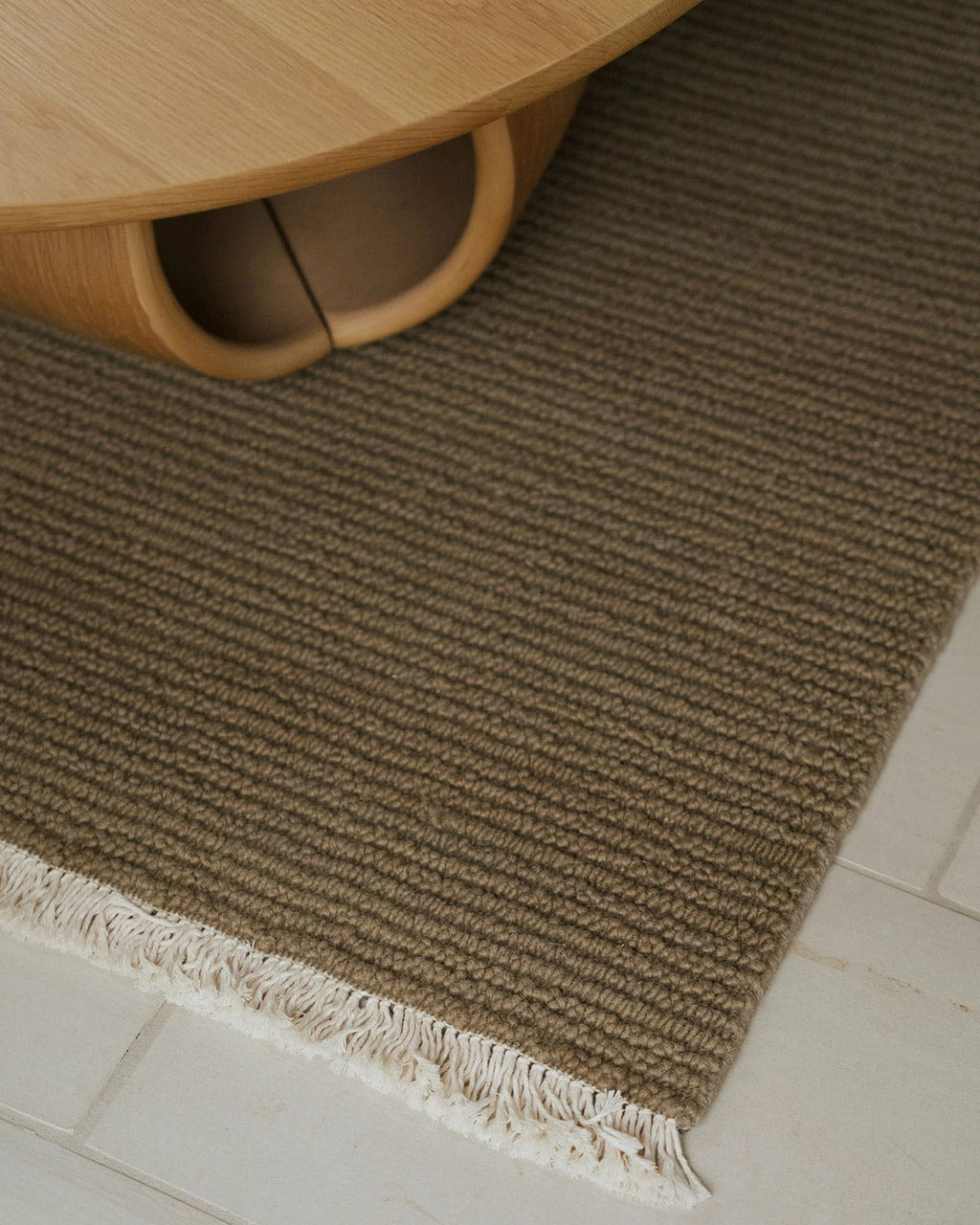 Brown textured rug with white fringe on a light wooden floor.