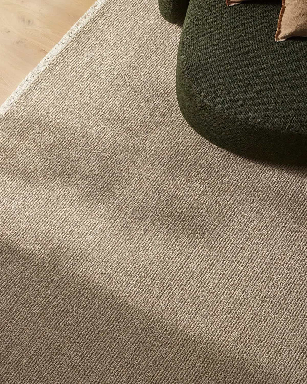 Close-up of a textured beige carpet with a green chair corner.