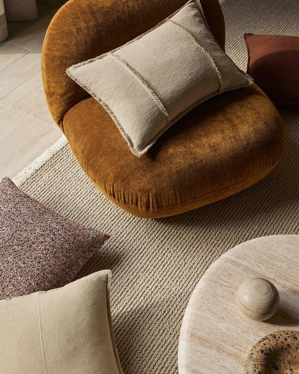 Round brown cushion with a beige pillow on a textured camel beige floor rug