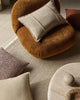 Round brown cushion with a beige pillow on a textured camel beige floor rug
