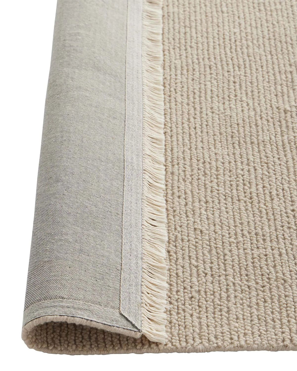 Close-up of a beige textured rug with a visible fringed edge, flipped up to show the underside, on a white background