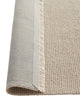 Close-up of a beige textured rug with a visible fringed edge, flipped up to show the underside, on a white background