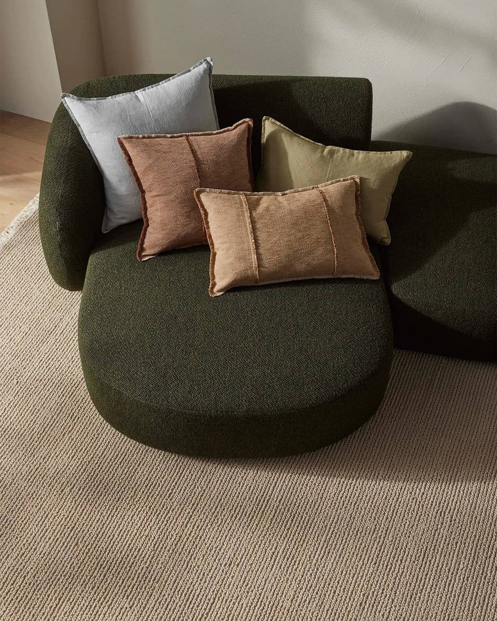 Green modular sofa with cushions on a neutral beige textural floor rug