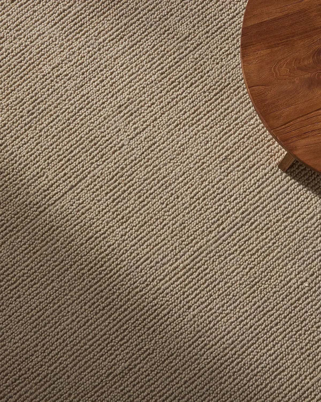 Close-up of a textured beige floor rug with a wooden table corner.