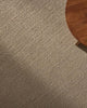 Close-up of a textured beige floor rug with a wooden table corner.