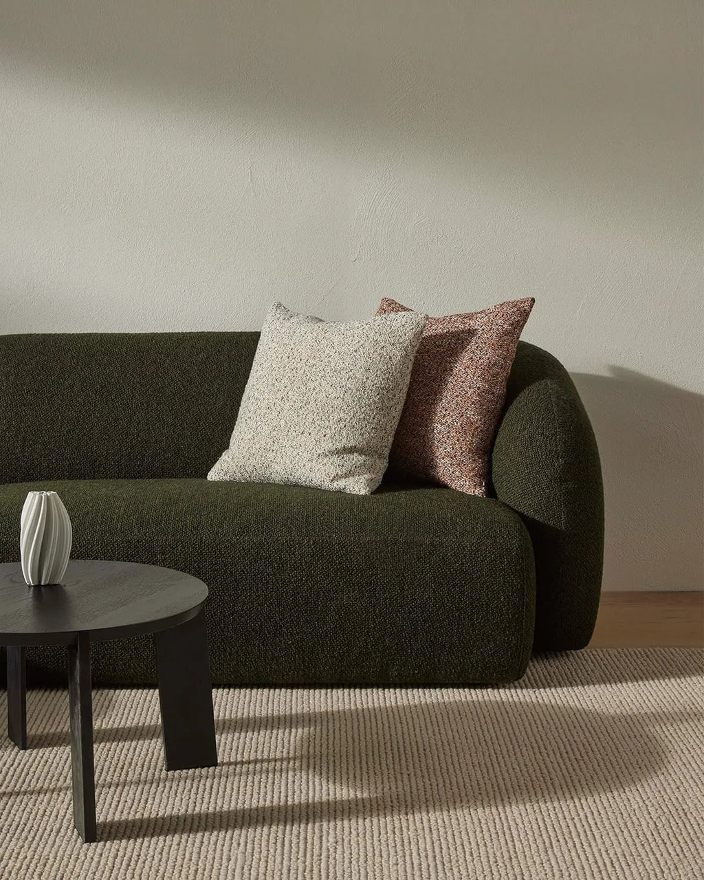 Green sofa with decorative pillows in a minimalistic room with a textured beige floor rug