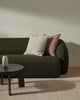 Green sofa with decorative pillows in a minimalistic room with a textured beige floor rug