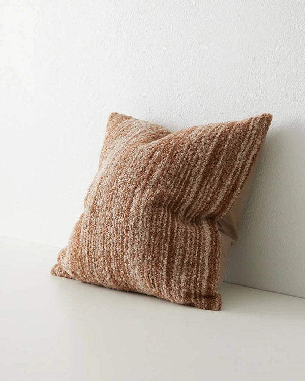 A textural, woven cushion in warm brown tones, seen at three quarter view