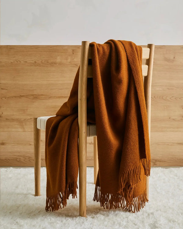 Weave Home wool throw blanket in colour 'spice' - a warm brown, draped over a chair