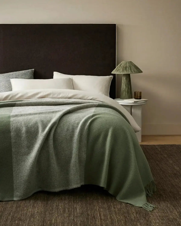 A soft green and grey wool throw in a large size at the end of a bed