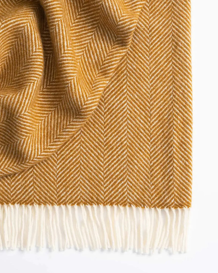 A thick and cosy throw blanket, with a herringbone design, in a rich amber colour, by Weave Home