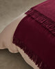Weave Home wool throw blanket in colour 'rhubarb' - a rich deep red, shown on the end of a bed