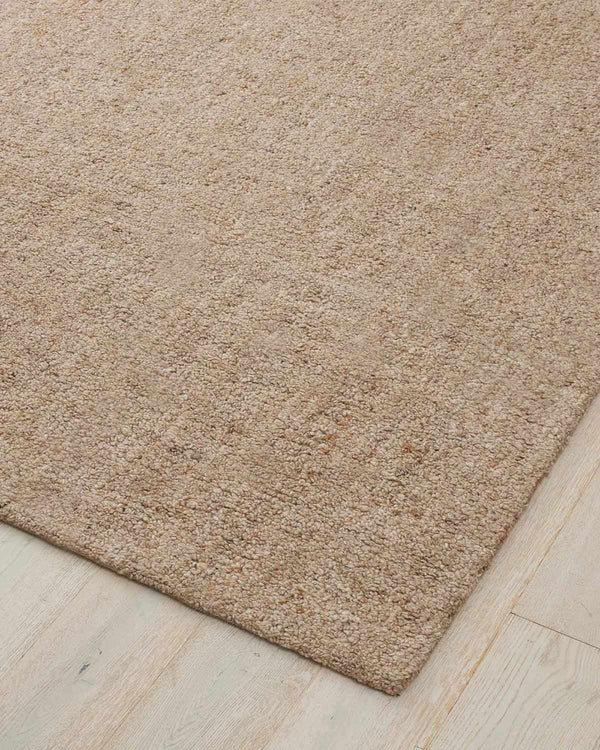 A corner image of a warm beige loop pile textural wool blend floor rug. 