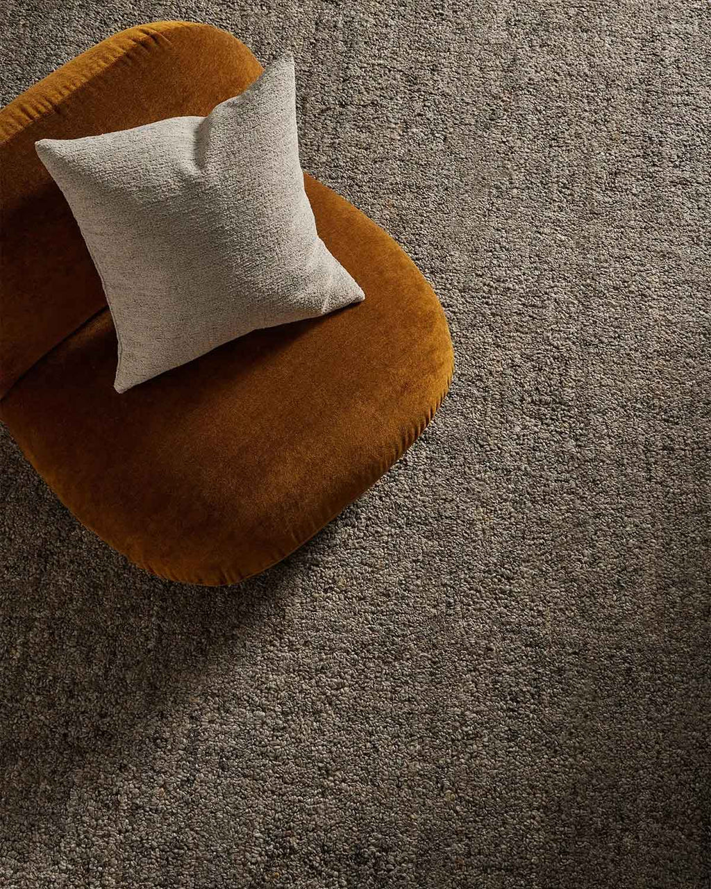 An amber toned armchair with a cream cushion on top of a shale grey textural wool blend floor rug. 