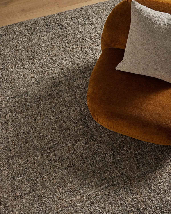 An ochre armchair on a textural slate toned charcoal floor rug with a textural loop piling in a durable wool blend. 